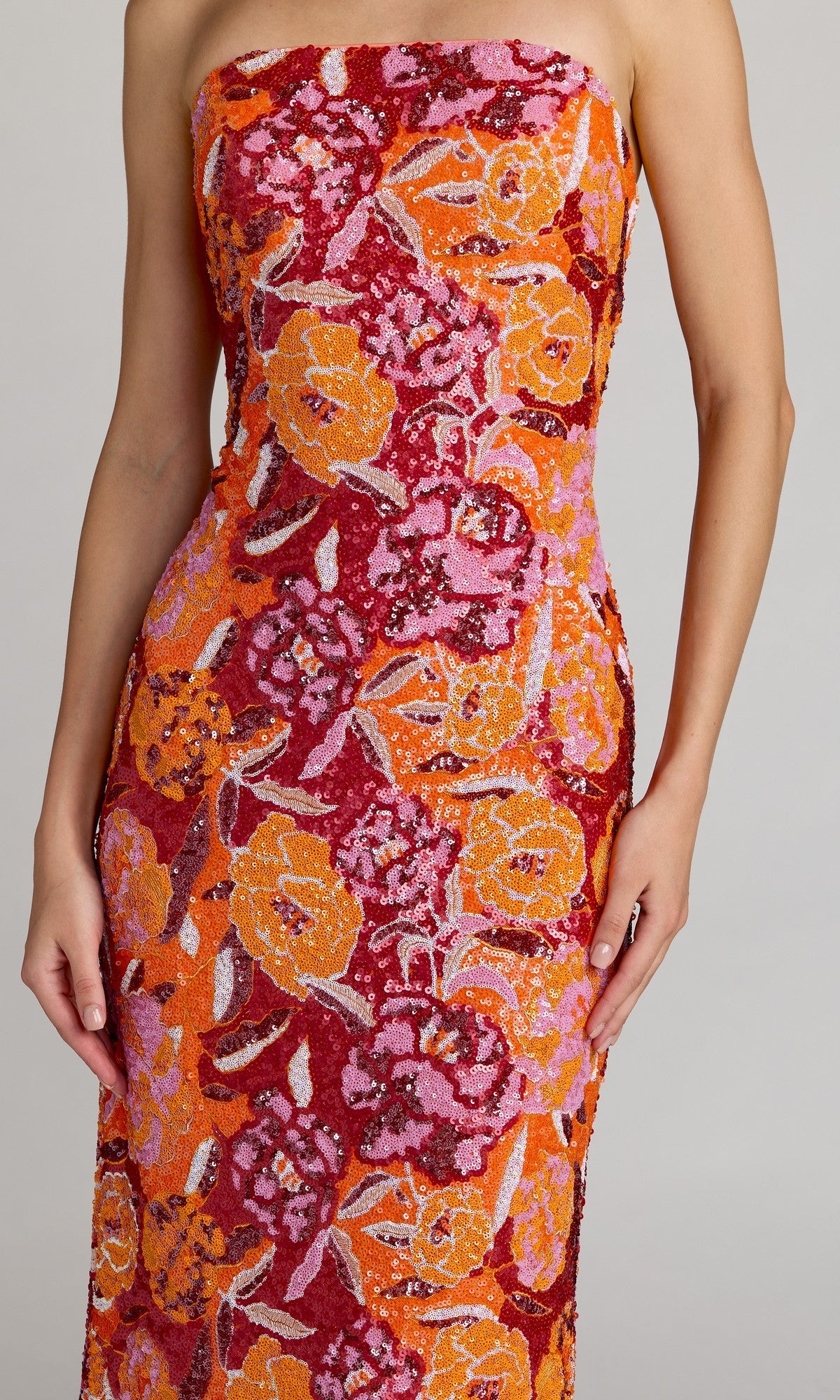 Wearing the Tea-Length Party Dress: Mac Duggal 56385, which features a strapless design and a lively red, orange, and pink floral pattern, a person stands against a plain background.